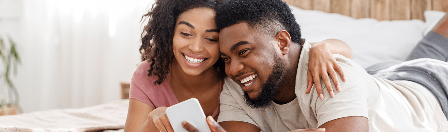 Happy Black Couple Using Smartphone On Bed EHCFRST